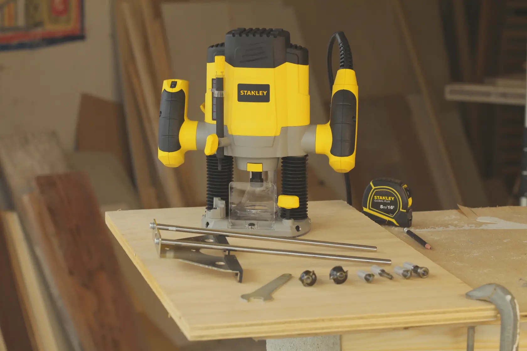 Photo of STANLEY SRR1200-AR plunge router with yellow and black design, accessories, and measuring tape on wood.