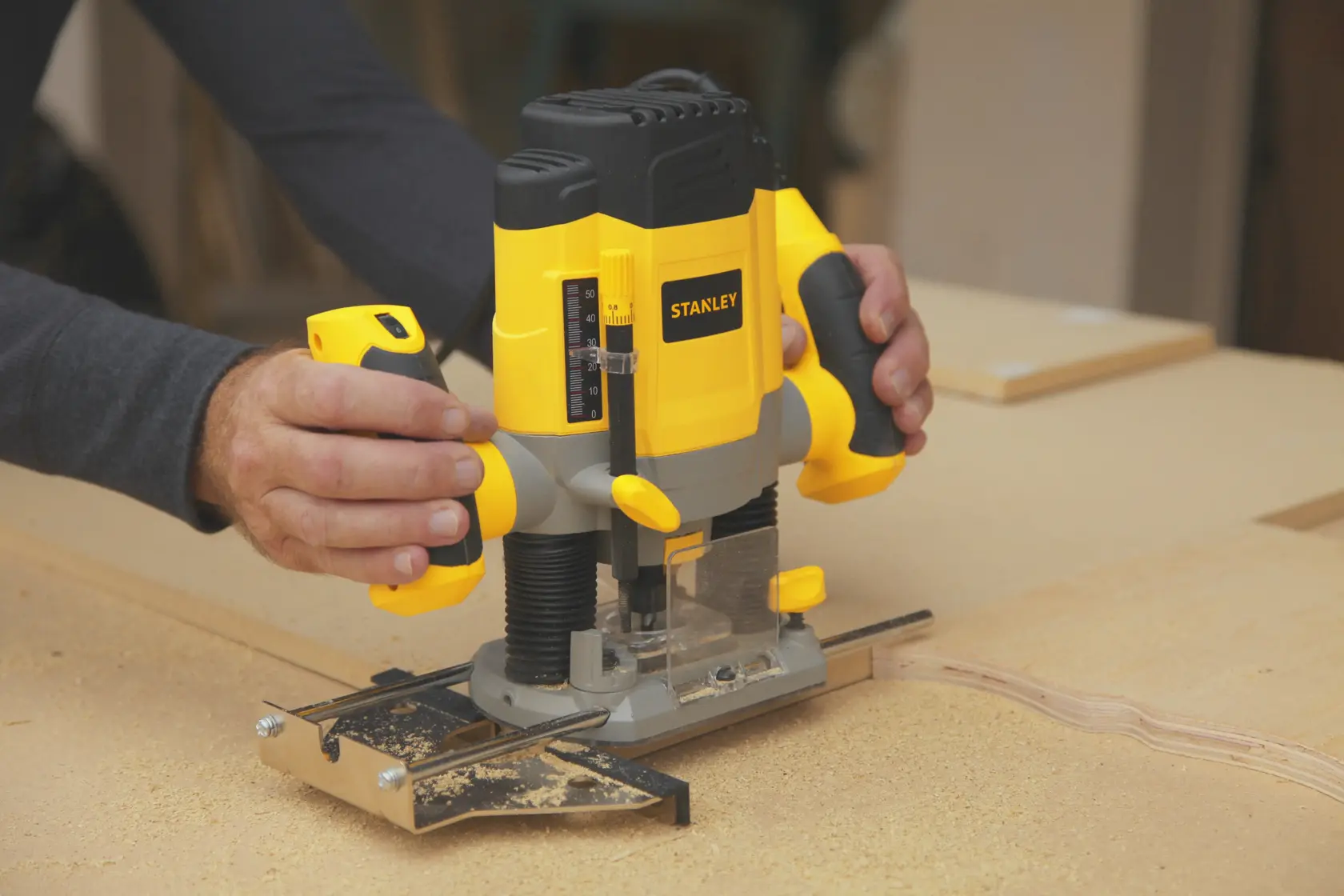 Photo of STANLEY SRR1200-AR plunge router in use on wood, yellow and black design, handled by a person.