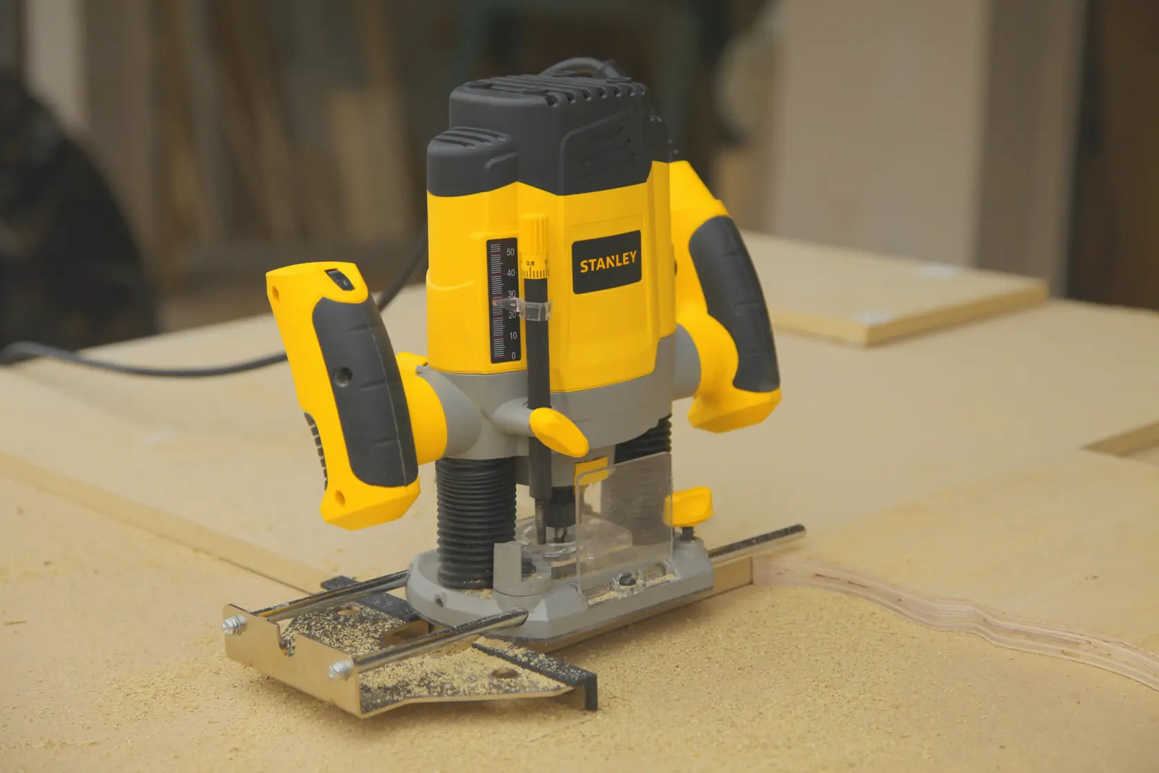 Photo of STANLEY SRR1200-AR plunge router with yellow and black body on wood surface in workshop.