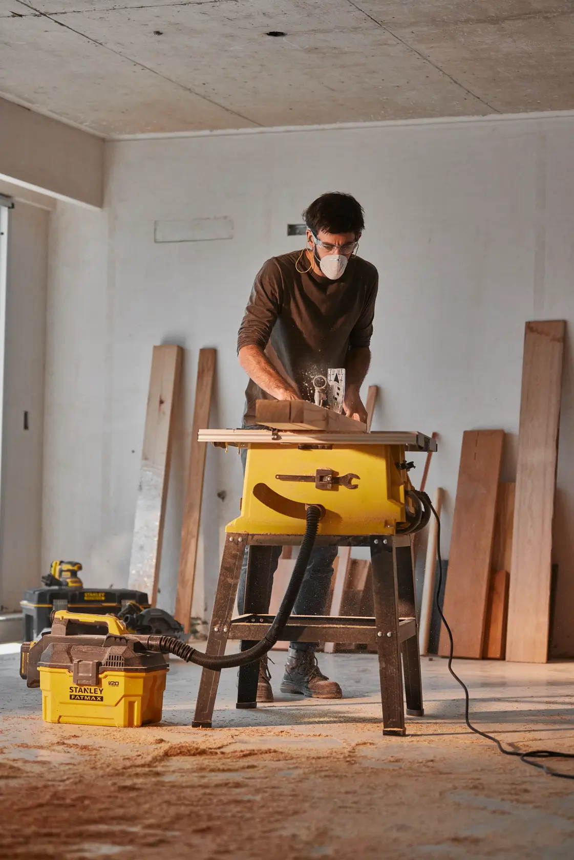 STANLEY SST2001-B2 vacuum cleaner connected to table saw in workshop with wooden planks in background, side angle.