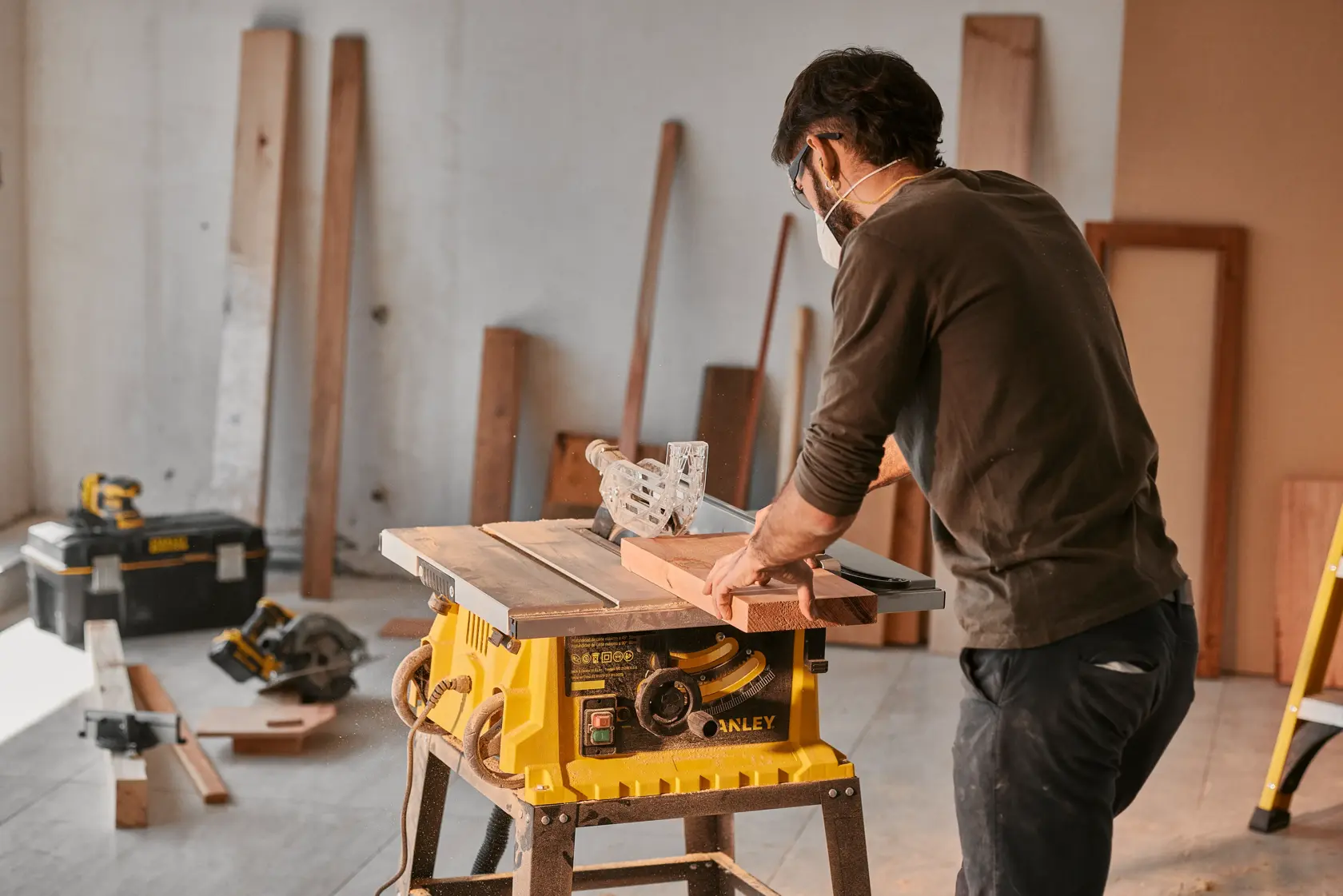 STANLEY SST2001-B2 table saw in use on a workshop floor, person cutting wood with safety equipment.