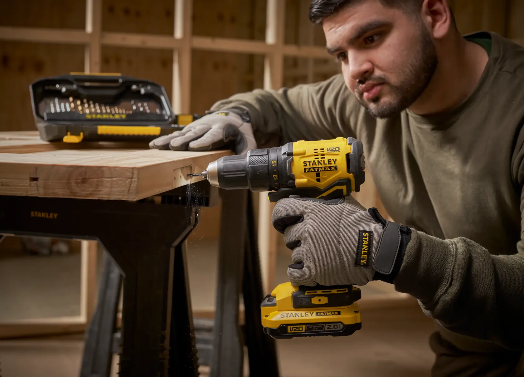 Stanley STA7184 cordless drill in use with drill bit set on wooden workbench, person wearing Stanley gloves.