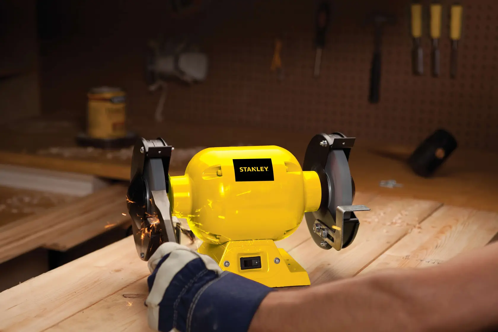 STANLEY STGB3715 bench grinder, yellow, used on a wooden workbench with sparks, side angle.