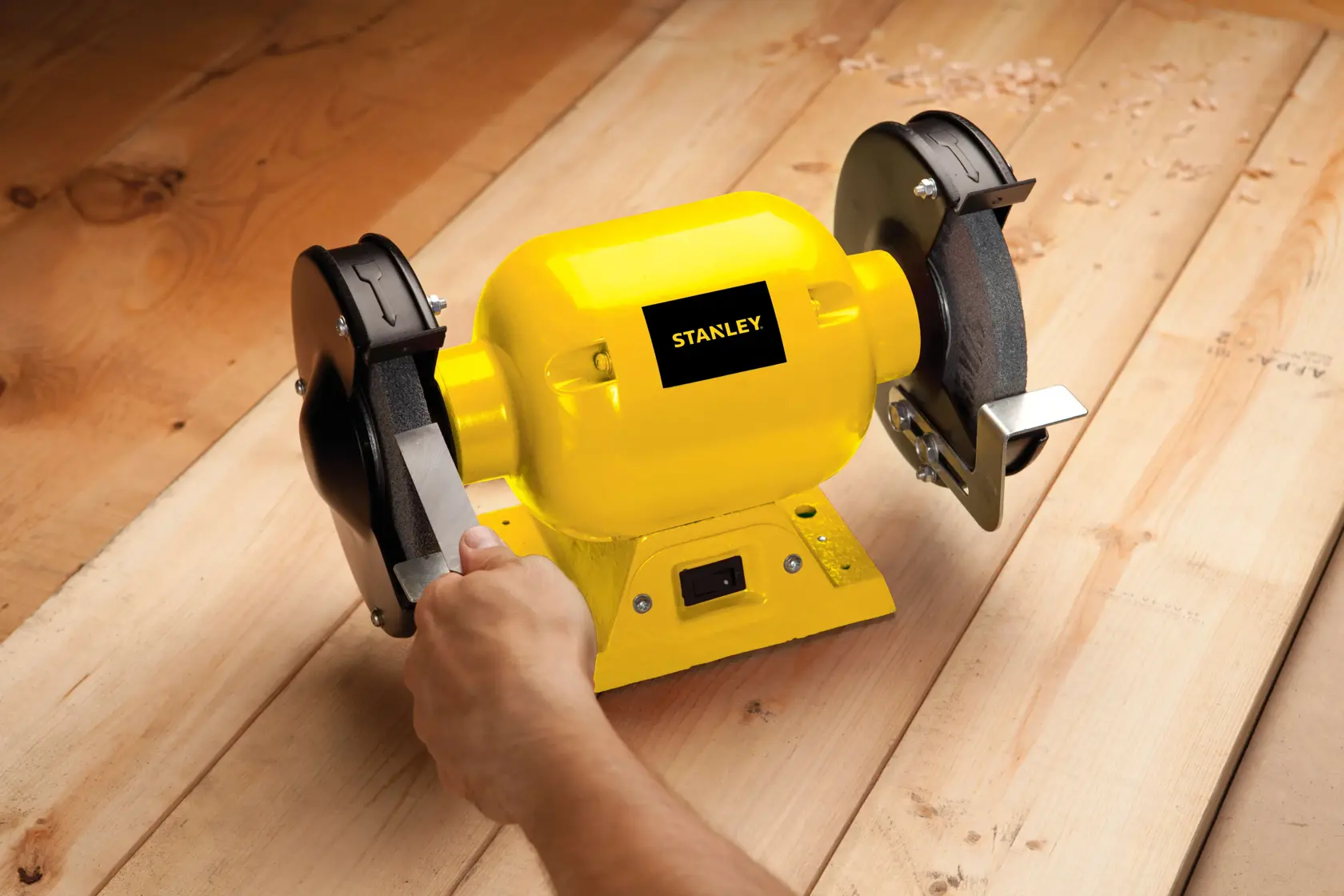 STANLEY STGB3715 yellow bench grinder in use on wood surface, close-up side view.