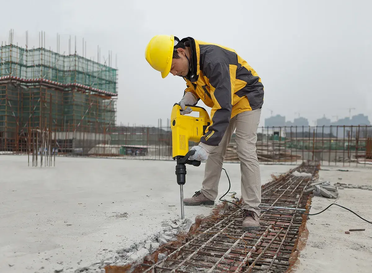 STANLEY STHM10K demolition hammer in use at a construction site, worker breaking concrete.