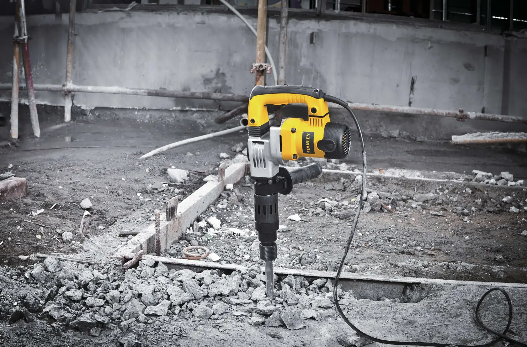 STANLEY STHM5KH demolition hammer drilling concrete rubble, yellow and black power tool at construction site.