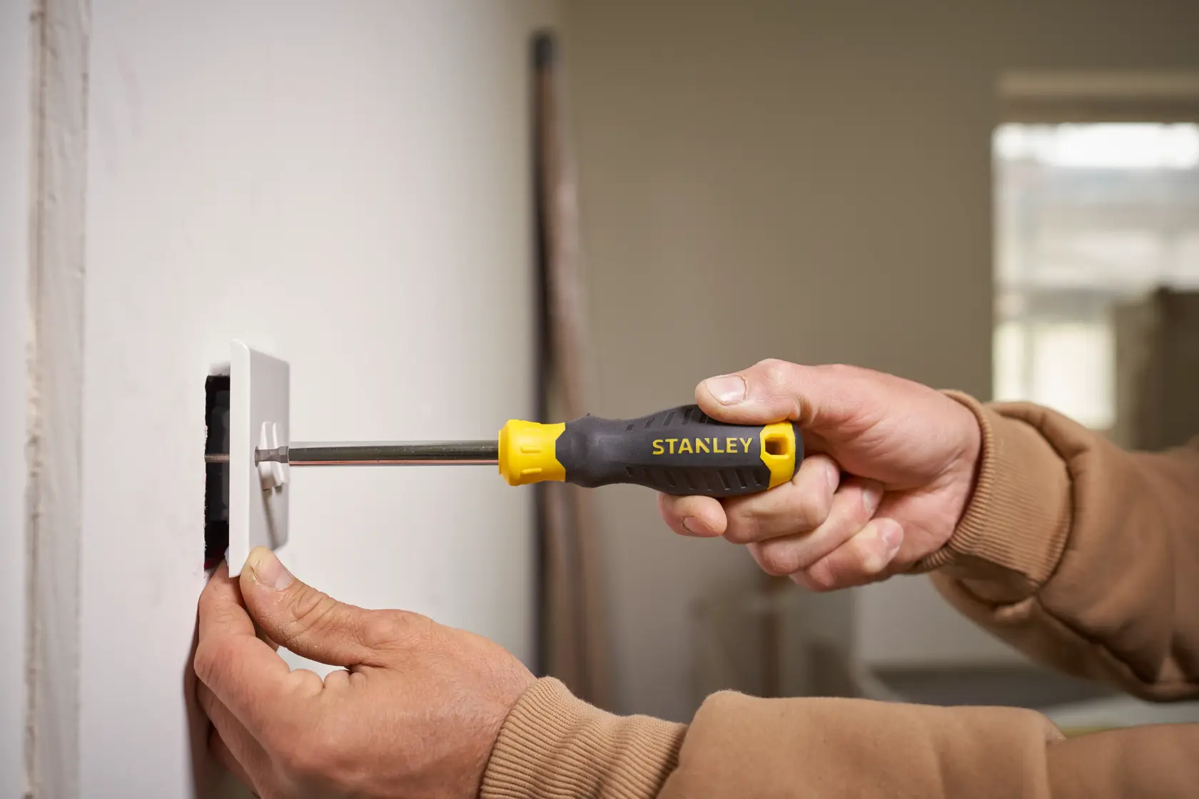 Stanley STHT0-70885 screwdriver with yellow-black handle used to install wall plate, close-up photography.