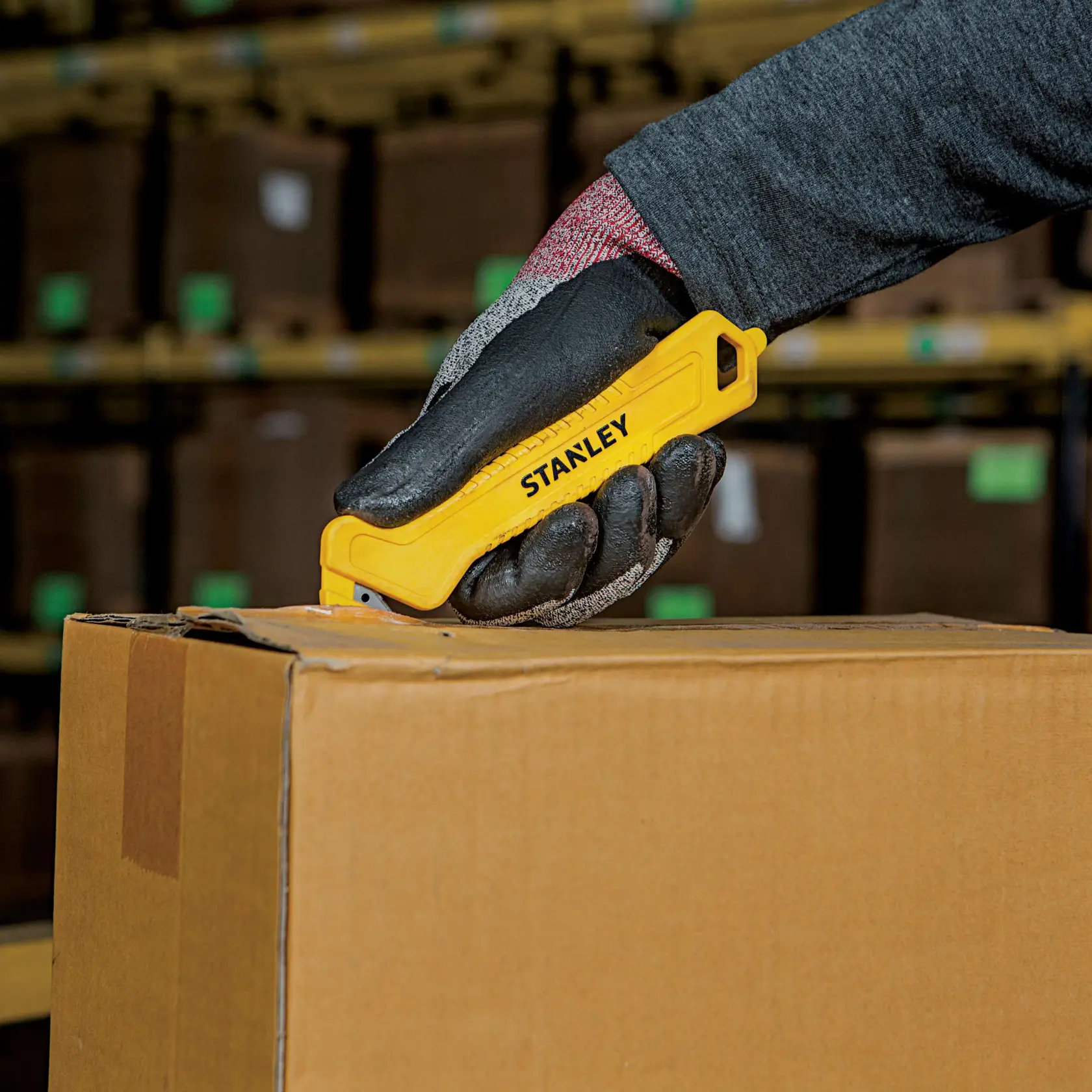 Photo of STANLEY STHT10355 yellow safety utility knife cutting cardboard box in warehouse setting.