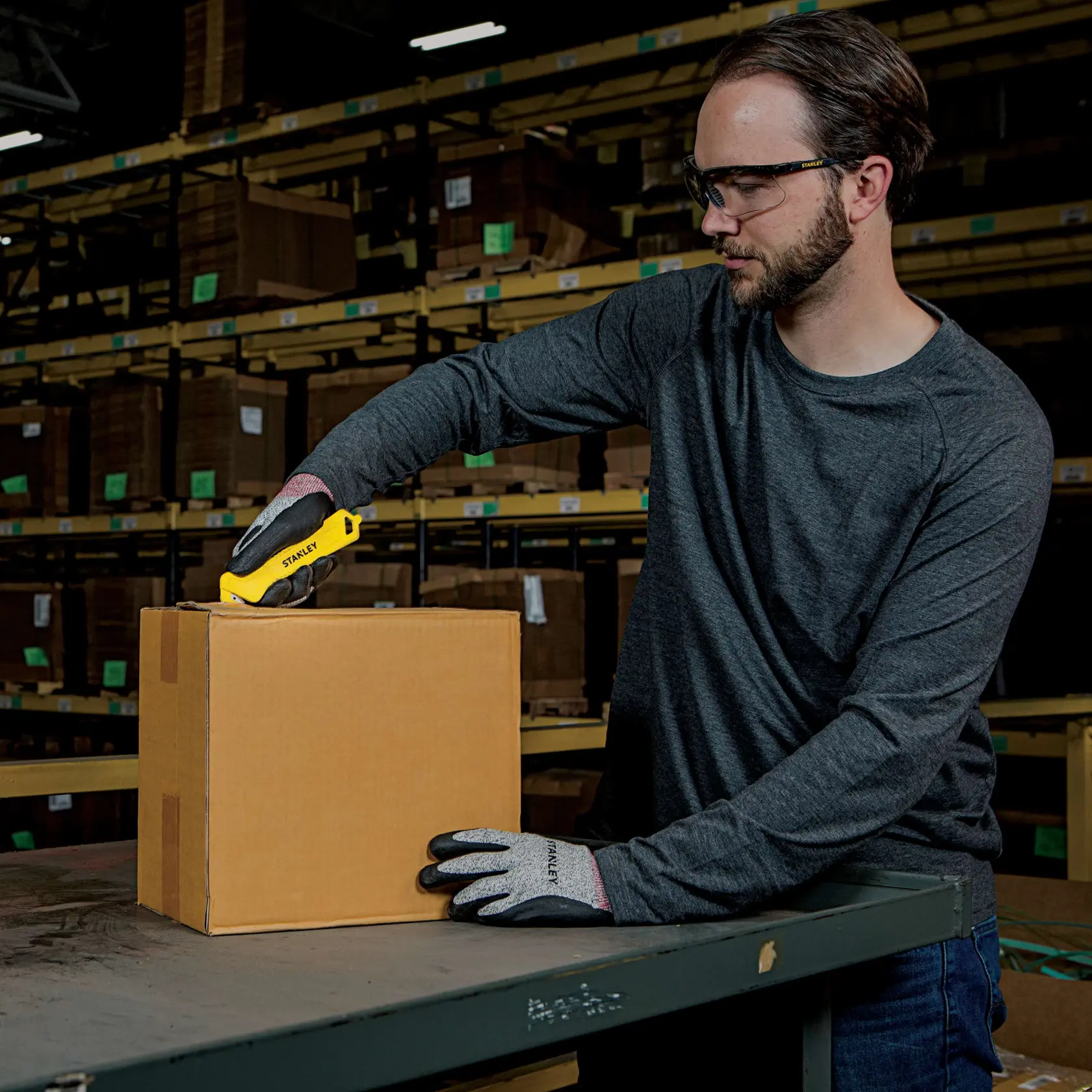 Stanley STHT10355 utility knife used to open a cardboard box on a warehouse table.