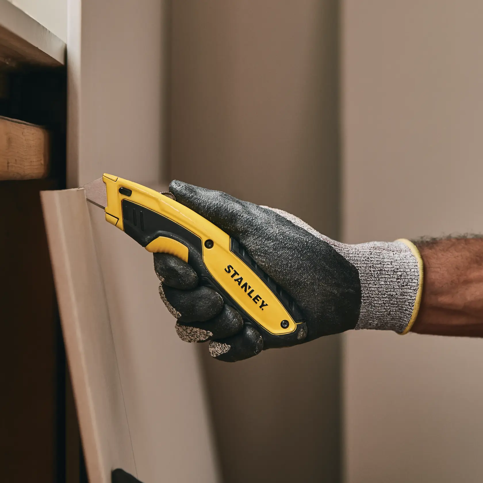 Stanley STHT10479-0 utility knife held in gloved hand, cutting a panel. Photography product category.