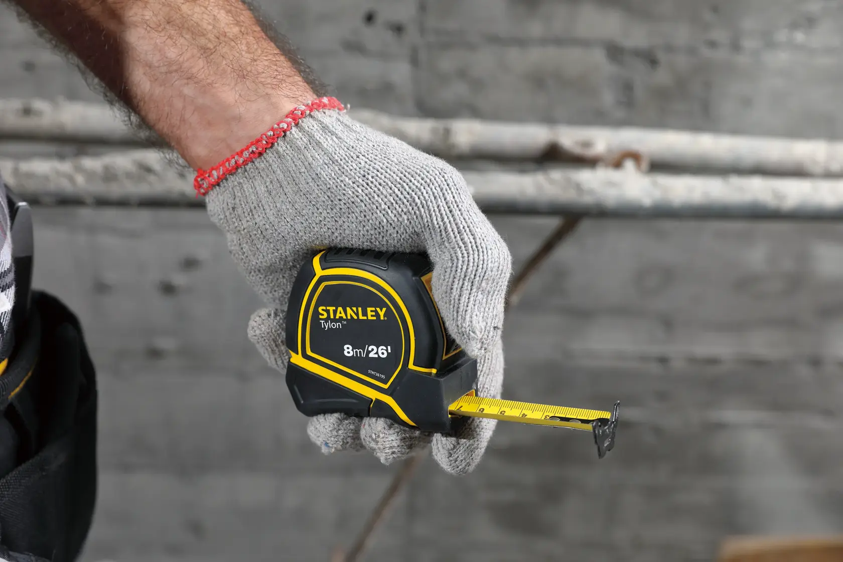 Photo of a gloved hand holding a STANLEY STHT36195 tape measure, yellow and black, partially extended.