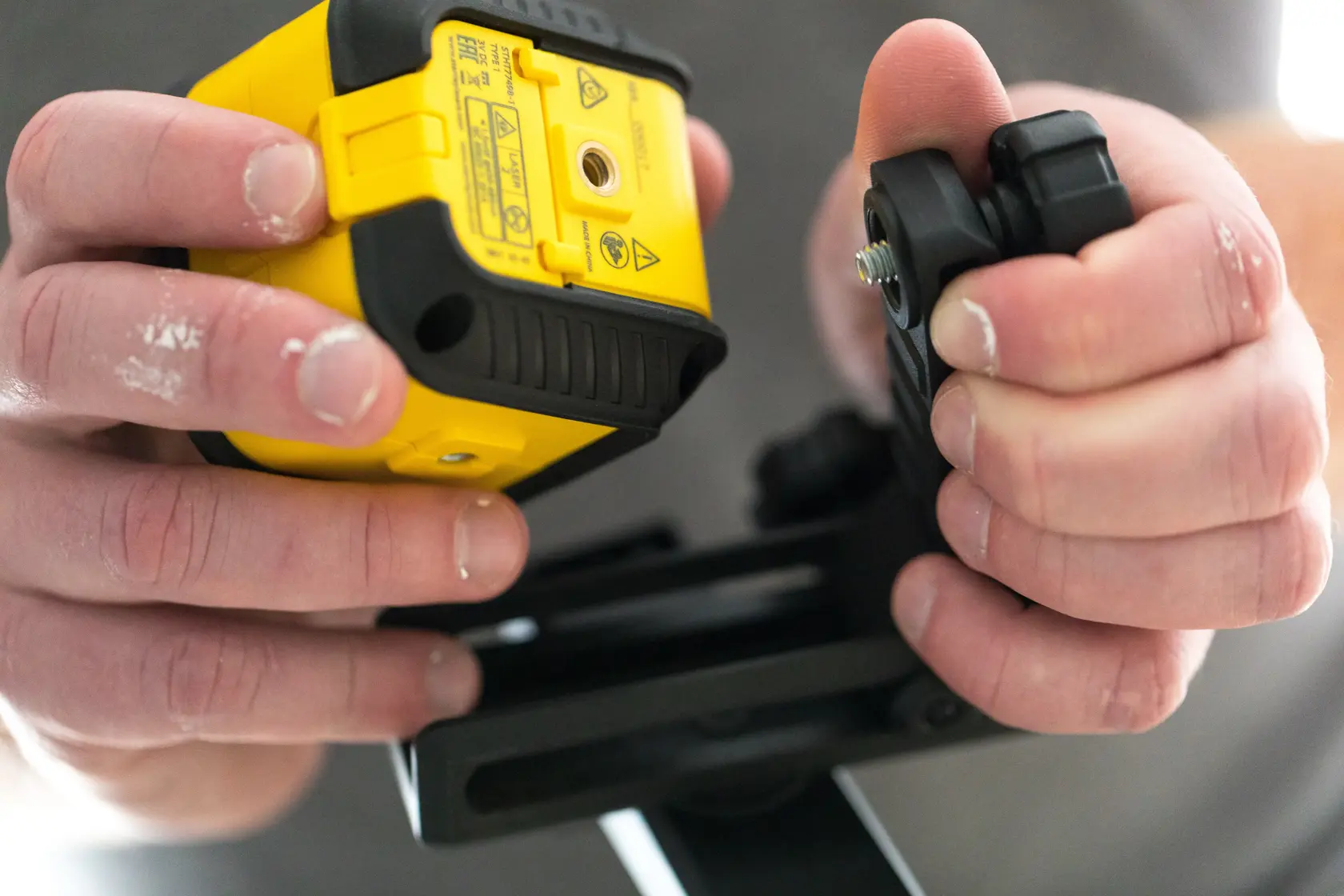 STANLEY STHT77498-1 photography close-up of hands assembling yellow laser level device and black mount