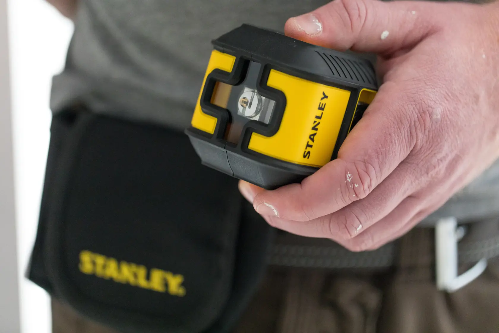 STANLEY STHT77498-1 yellow and black laser level held in hand, tool pouch visible on waist.