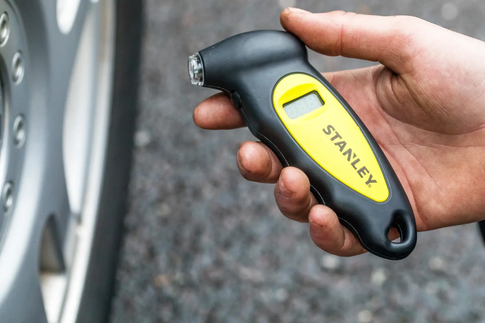 Stanley STHT80874-0 digital tire pressure gauge handheld near car wheel, black and yellow design.