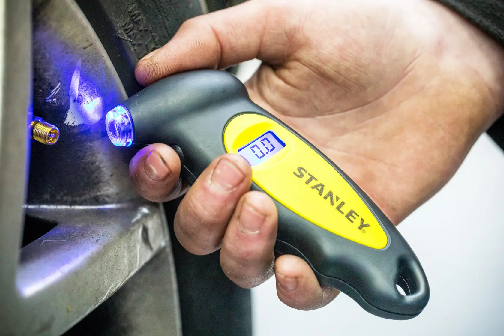 Stanley STHT80874-0 digital tire pressure gauge with blue LED, handheld near tire valve.