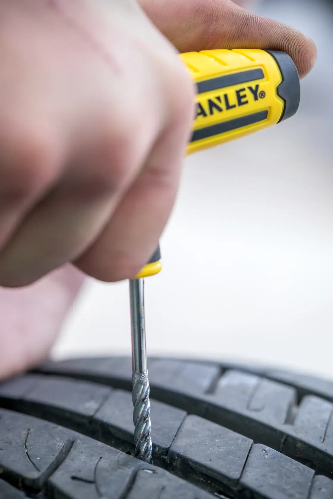 STANLEY STHT80891-0 tire repair tool with yellow handle used on black car tire, close-up.