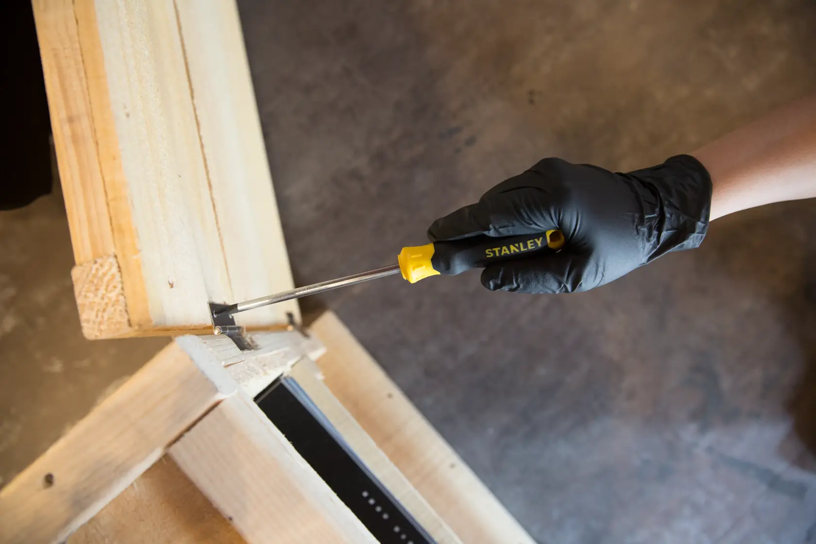 STANLEY STMT60811-8 screwdriver with yellow and black handle used to fasten a screw in wood, top view.