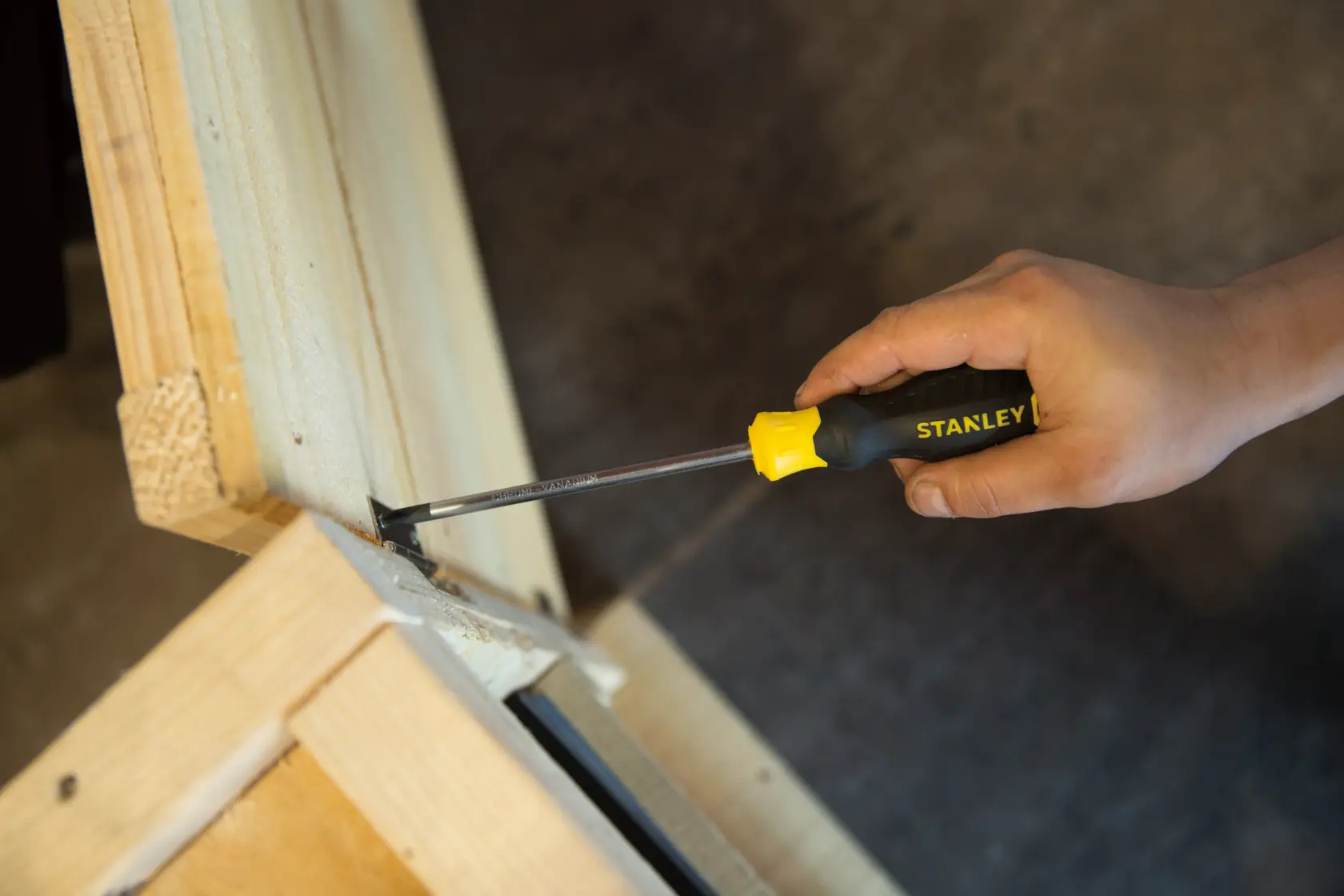 Photo of STANLEY STMT60811-8 flathead screwdriver used on wooden frame, black and yellow handle visible.