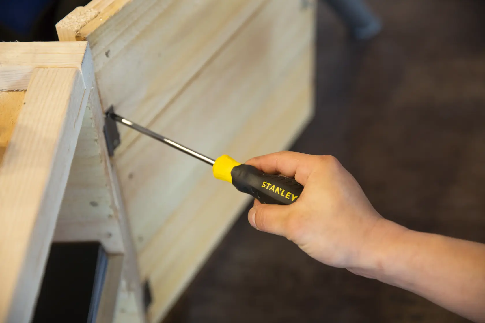 Stanley STMT60811-8 screwdriver with yellow and black handle used on wooden furniture, close-up.