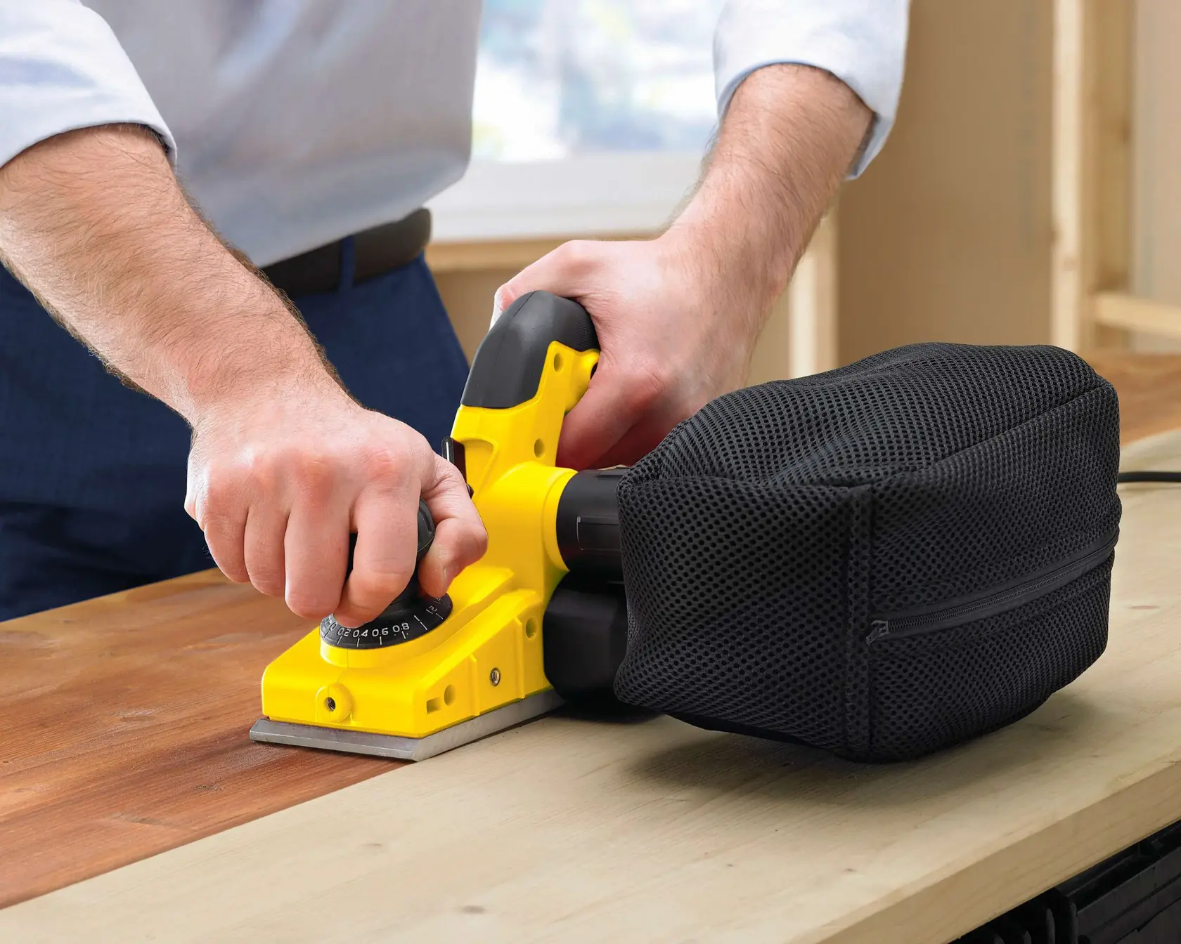 Photo of STANLEY STPP7502-B2 hand planer with black dust bag sanding wooden surface, close-up in use.