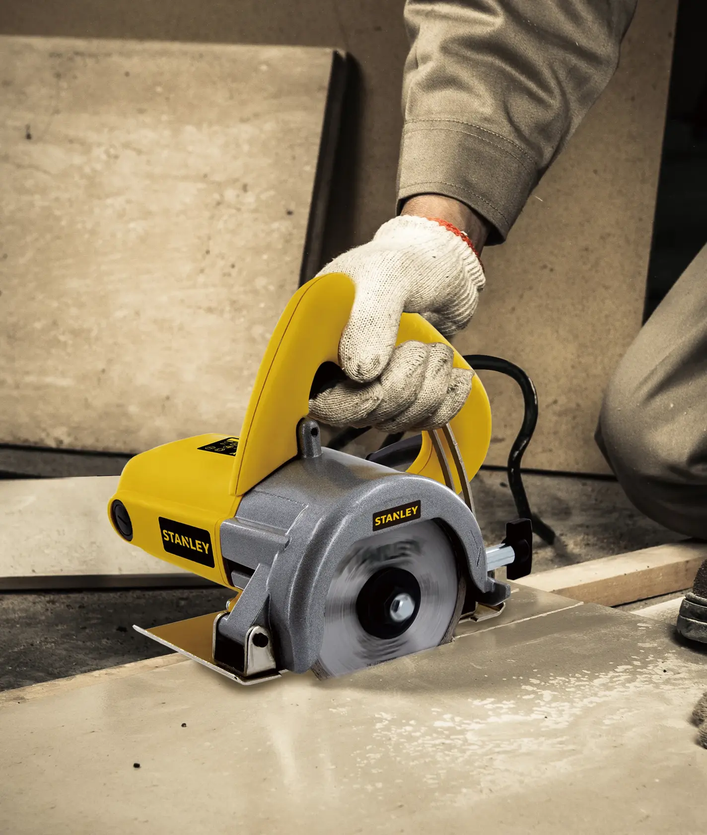Stanley STSP110 tile cutter in use, yellow and silver body, cutting ceramic tile on construction site.