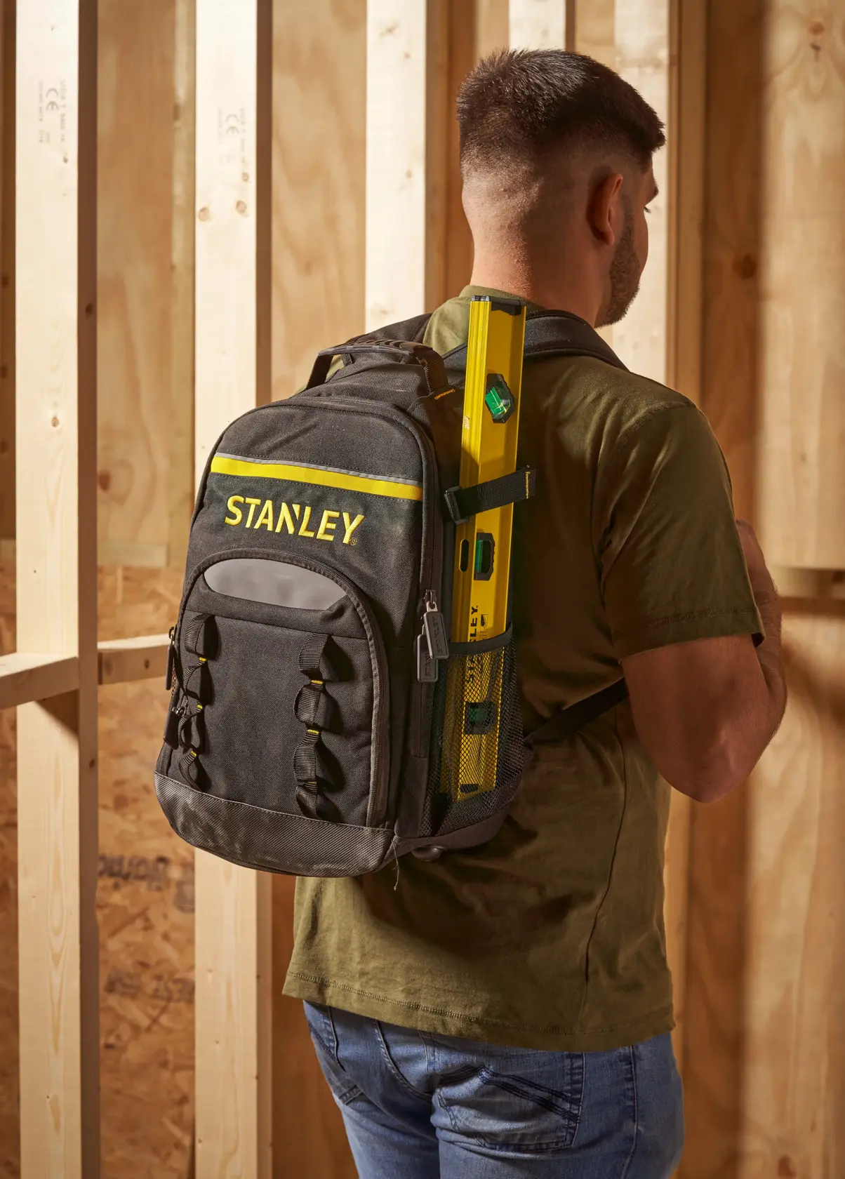 Stanley STST1-72335 black and yellow backpack worn by a man in a workshop, holding a level tool.