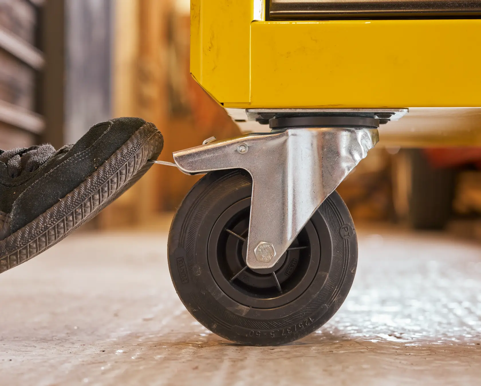 Photo of STANLEY STST74305-1 caster wheel with brake, attached to yellow tool chest, close-up side angle.