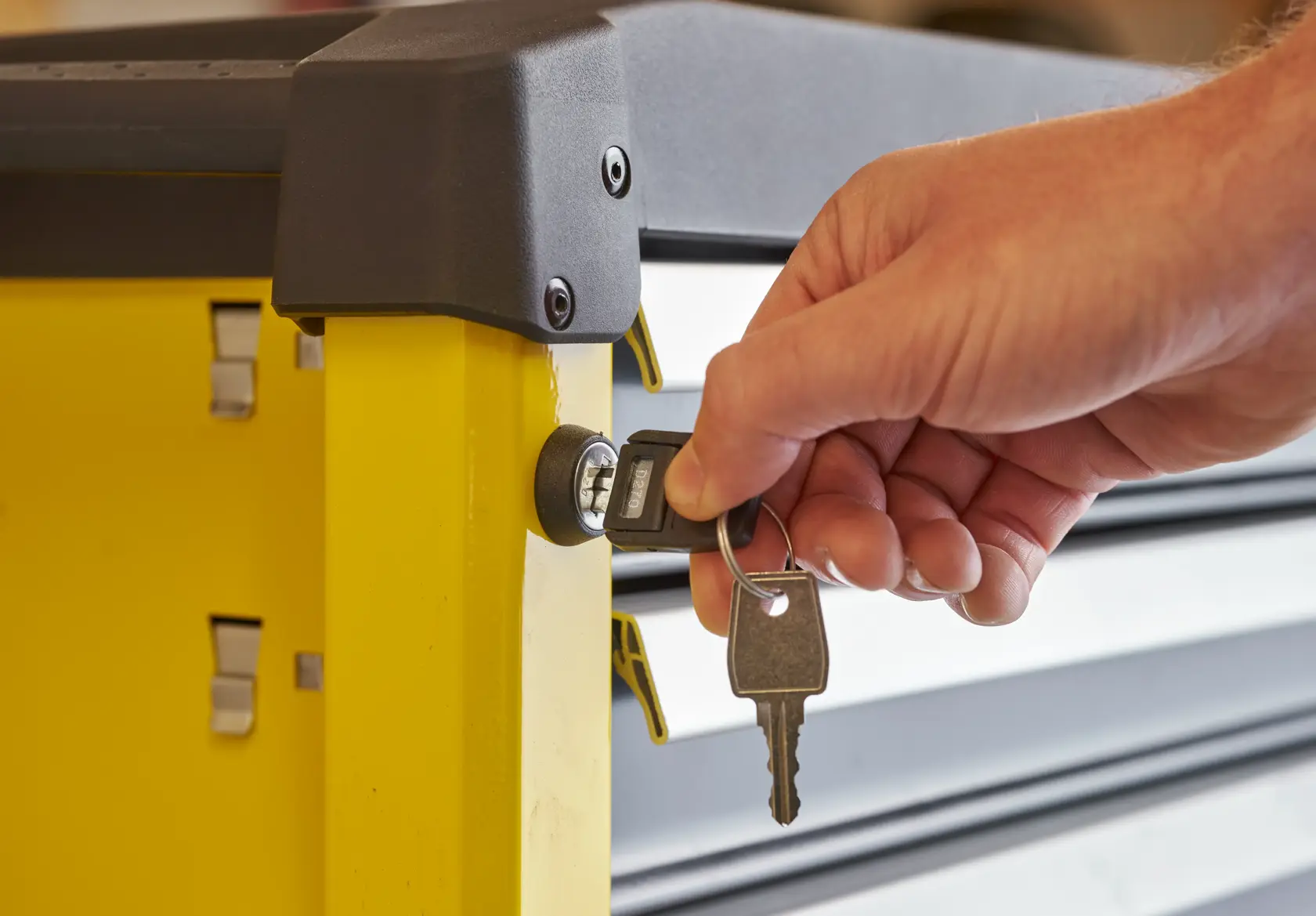 Photo of a hand locking a yellow STANLEY STST74305-1 tool chest with a key, close-up side view.
