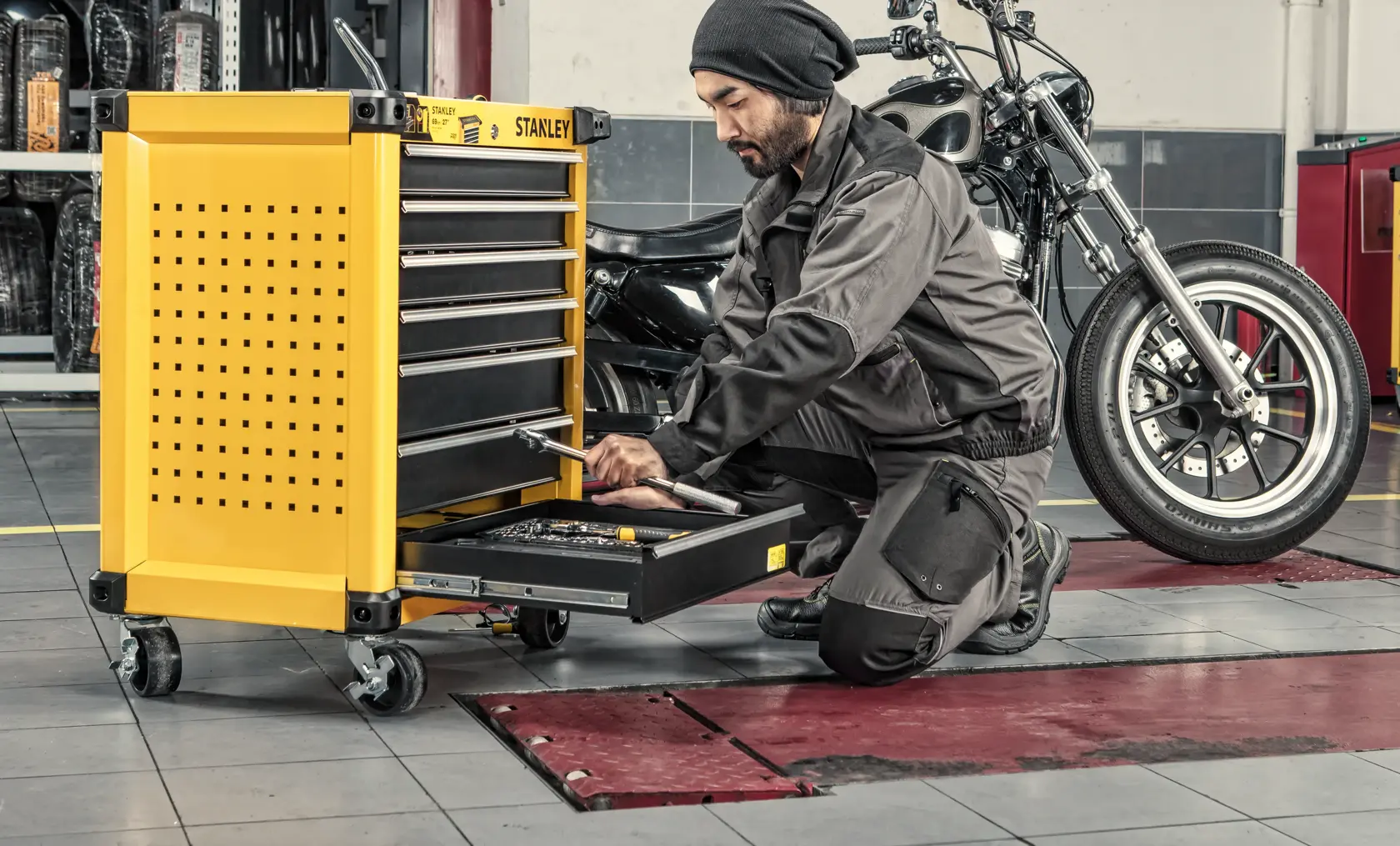 Stanley STST74306-8 yellow tool chest with drawers in workshop, mechanic using bottom drawer near motorcycle.