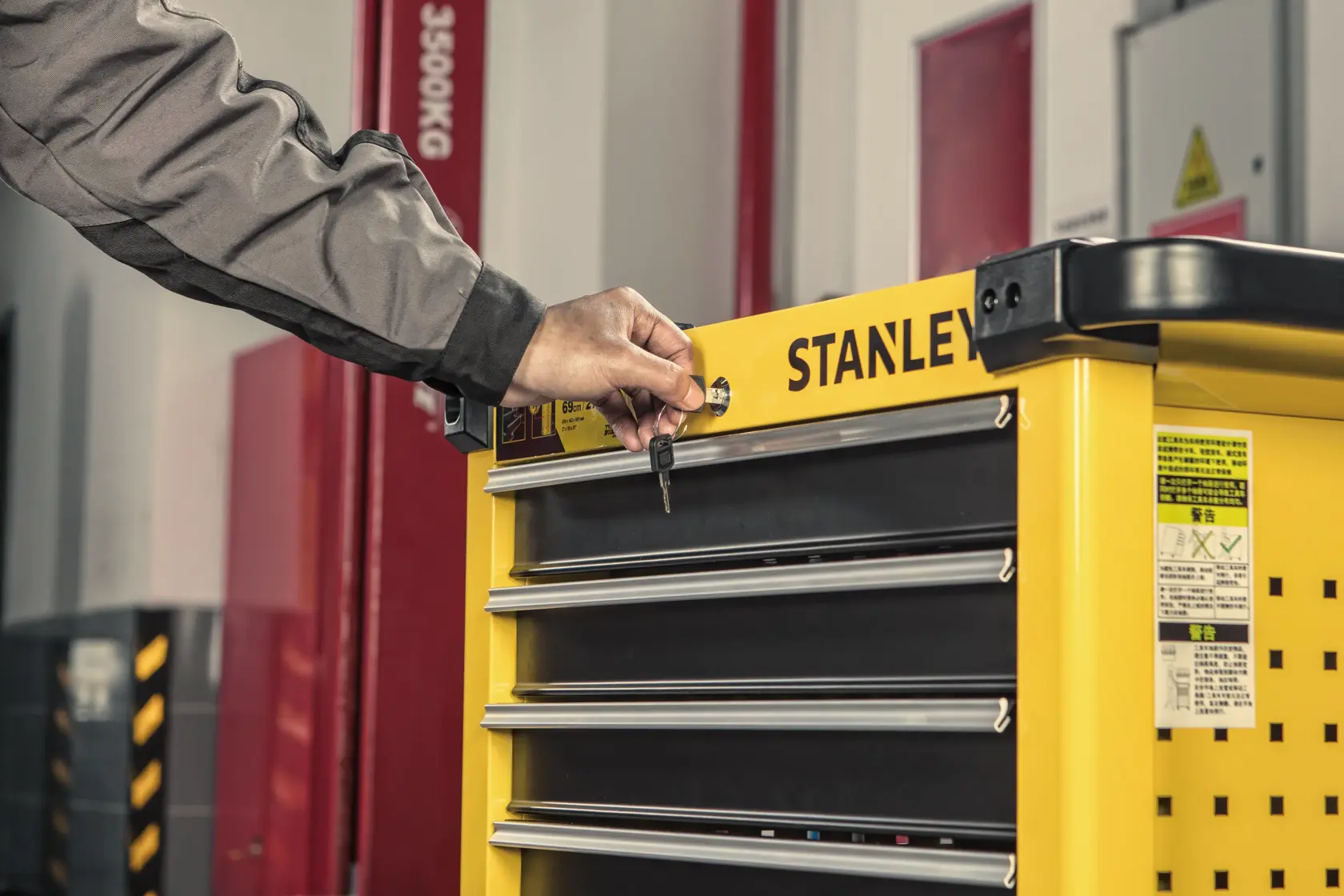 STANLEY STST74306-8 yellow tool chest with drawers, shown being locked with a key in workshop setting.