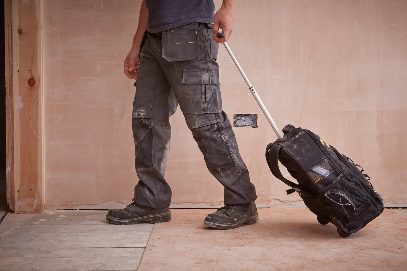 STANLEY STST83307-1 rolling tool backpack on construction site, side angle, black with yellow details.