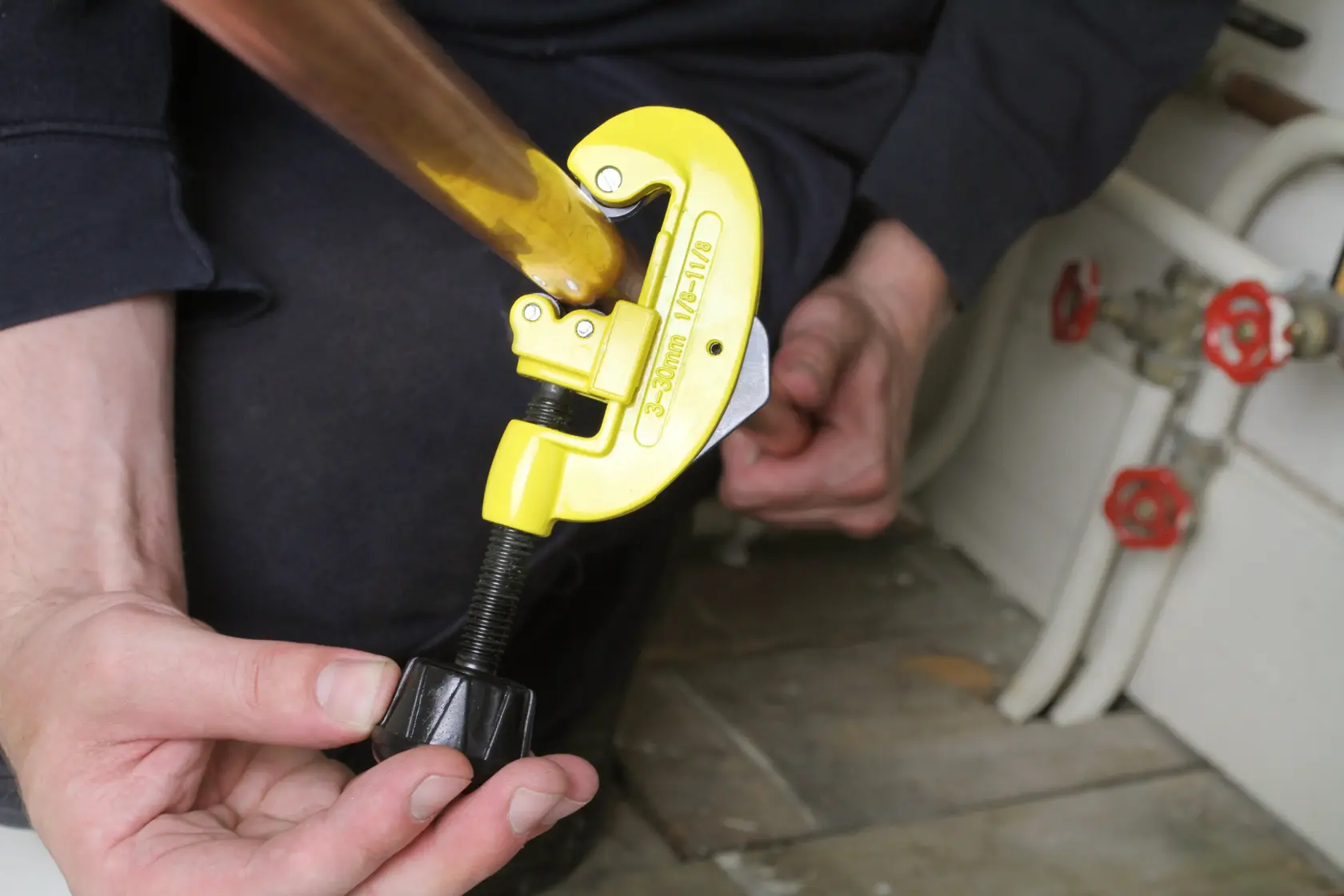 STANLEY 0-70-448 pipe cutter in use, yellow body on copper pipe, hands adjusting tool, plumbing context.