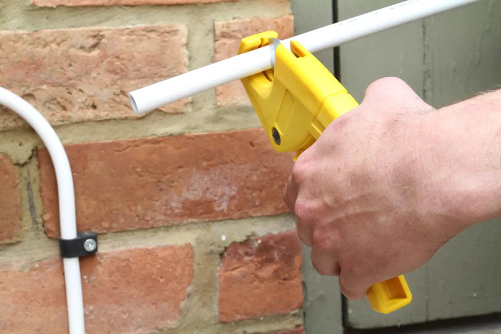 STANLEY 0-70-450 pipe cutter tool cutting white plastic pipe, close-up outdoor photography.