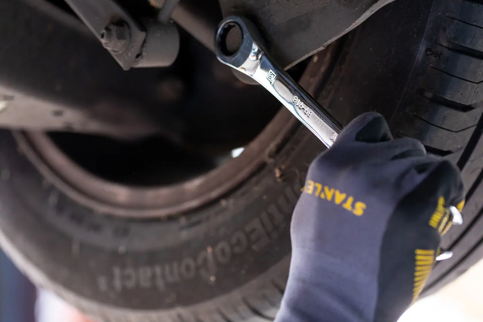 STANLEY STMT82847-0 wrench used on car wheel by gloved hand in close-up automotive context.